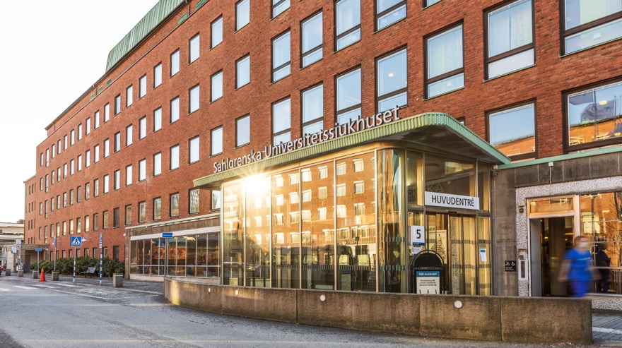Rexuma vårdrumspanel En modern tegelbyggnad med stora fönster, märkt Sahlgrenska Universitetssjukhuset. Entrén har en glasmarkis och en skylt med texten Huvudentré. Solljuset reflekteras på byggnaden och en person går i närheten.